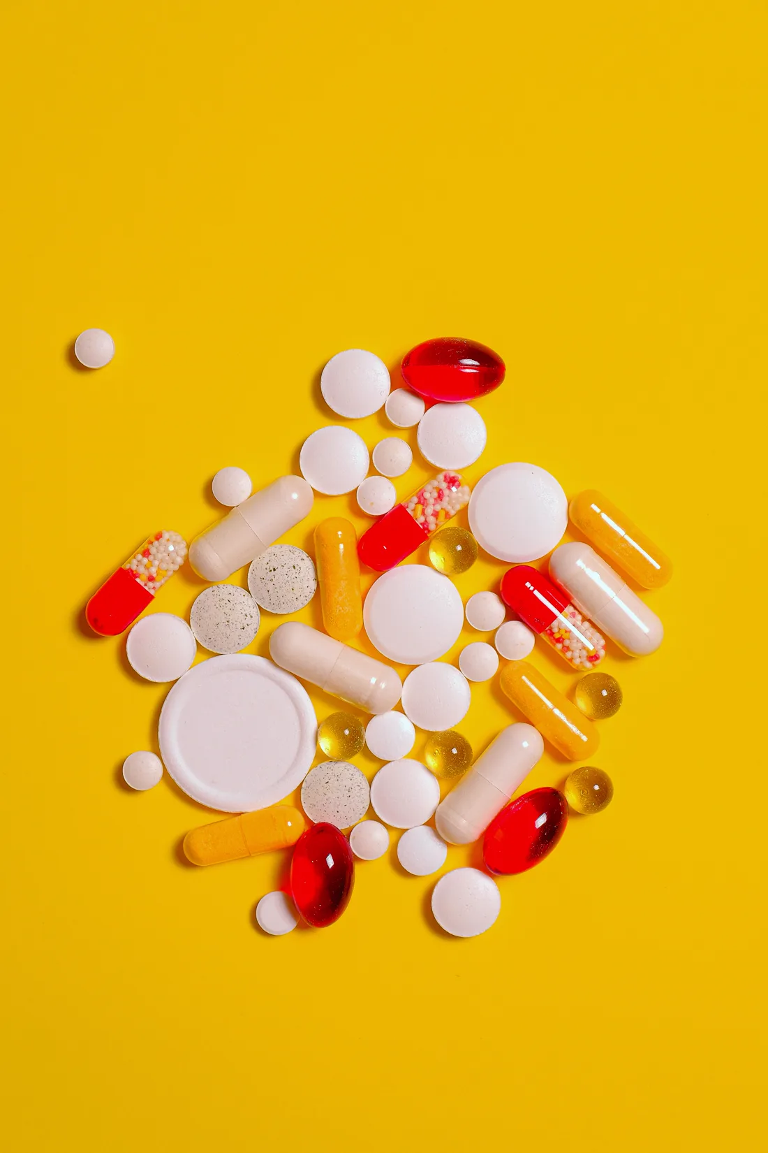 Assorted over-the-counter tablets and capsules on a yellow surface